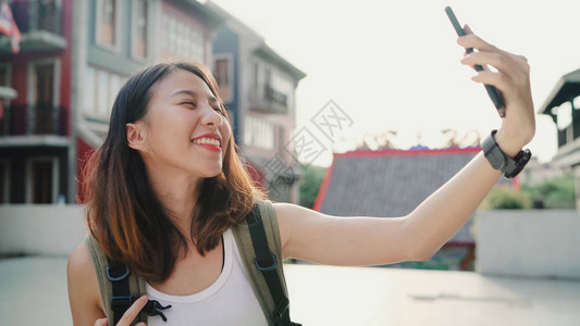 快乐美丽的年轻亚洲背包客博女在北京唐人街旅行时使用智能手机自拍生活方式背包背景图片