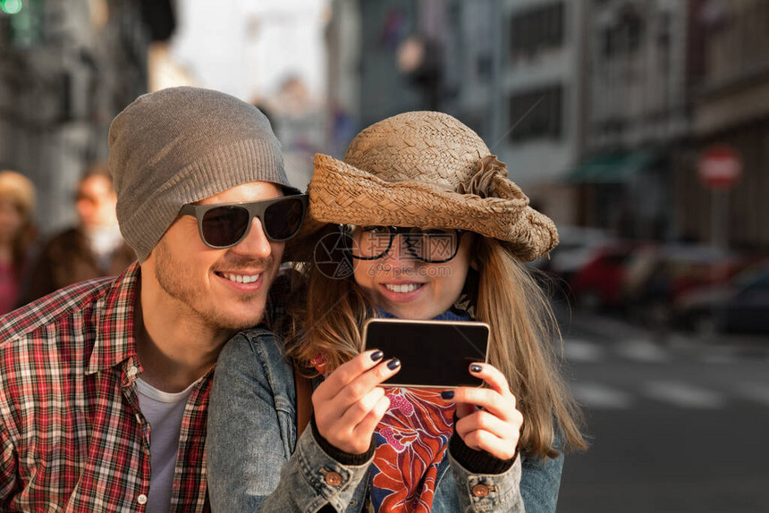 在城市环境使用智能手机拍摄照片的年轻旅游夫妇图片