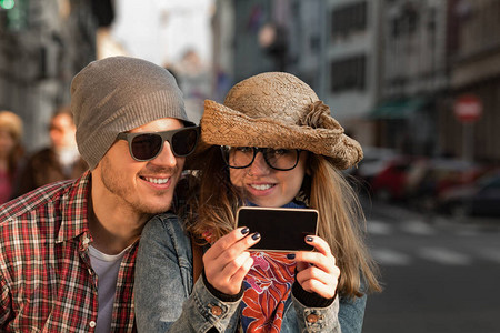 在城市环境使用智能手机拍摄照片的年轻旅游夫妇图片