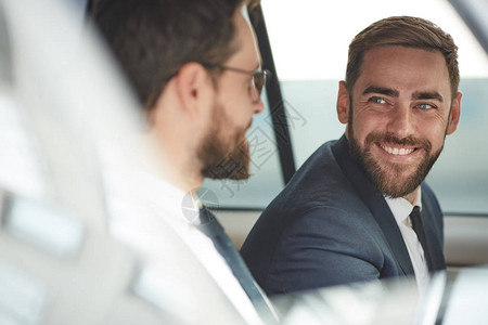 年轻快乐的商人与同事交谈坐在车里时图片