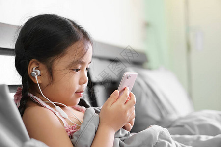 亚洲儿童或小女孩微笑时戴着耳机或耳机和闲聊在线学习或在家工作图片
