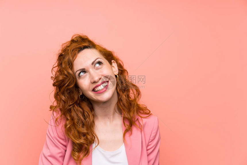 身穿西装的红发女人在孤立的粉红色墙图片