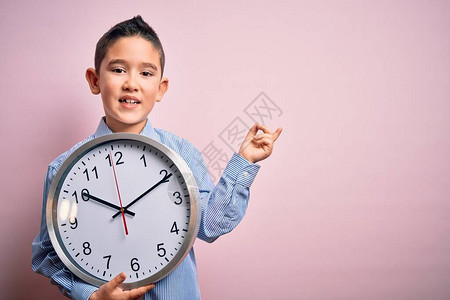 小男孩拿着大钟在孤立的粉红色背景上非常高兴地用手和图片