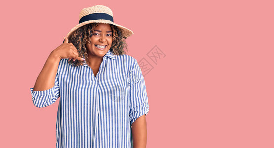 身戴暑期帽的年轻非洲加体型女微笑着用手和指做电话手势图片
