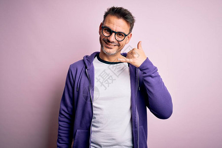 年轻英俊的男人穿着紫色运动衫和眼镜站在粉红色的背景上图片