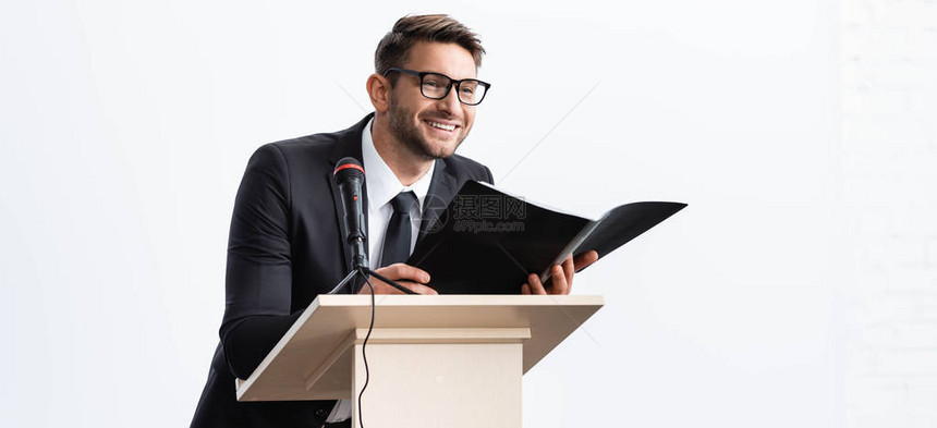 站在讲台上的Trune和在以白色为孤立地点的会议上持有文件夹时袖手旁观的笑图片