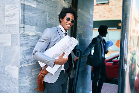 年轻英俊的非裔美国建筑师笑得很开心站在办公室门前拿着蓝图的脸上图片