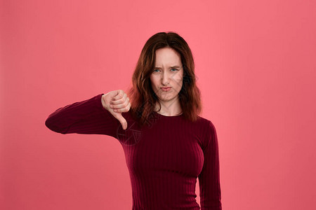 不幸的年轻女士站在黑暗粉红背景旁举起拇指下方的手势象征图片
