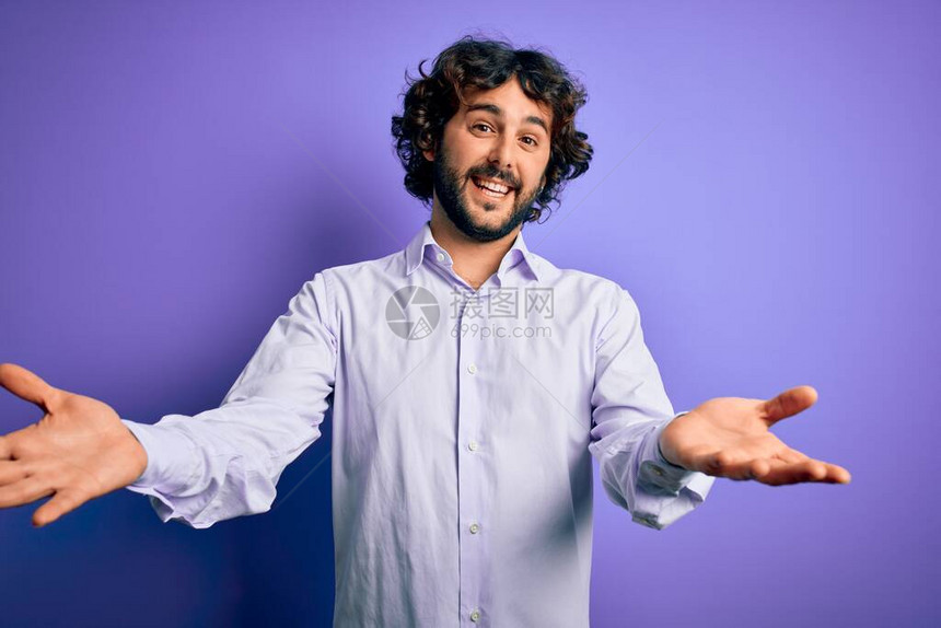 年轻英俊的生意人胡子穿衬衣站在紫色背景上微笑着欢笑着伸出手来给图片