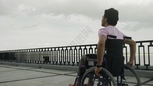 在轮椅上残疾的青年男子沿图片