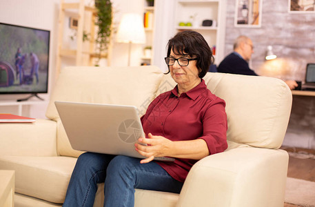 60多岁的老年妇女坐在沙发上用笔记本电脑的沙发上图片