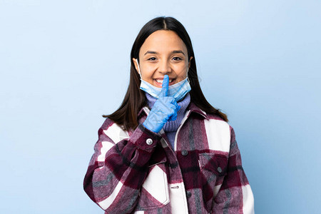 年轻的黑发混血女戴着面具和手套在孤立的蓝色背景上保护免受冠状的侵害背景图片