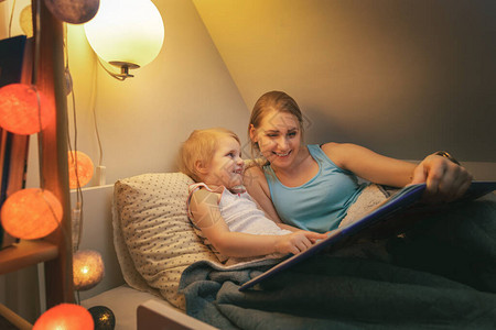 母亲和女儿在家睡觉前晚上一起阅读童话尾巴小说背景图片