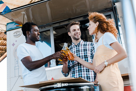快乐的多元文化男人在食品卡车附近与迷人的红发女人碰杯图片