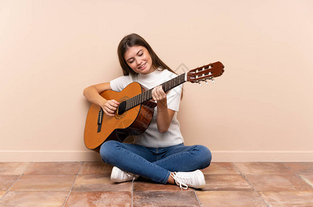 坐在地板上的吉他的年轻女子图片