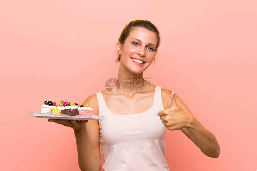 年轻金发美女拿着许多不同的小蛋糕拇指举起手来因图片