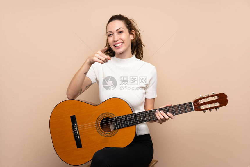 带着吉他的年轻女青年在孤立的背景点上弹吉他用自信图片