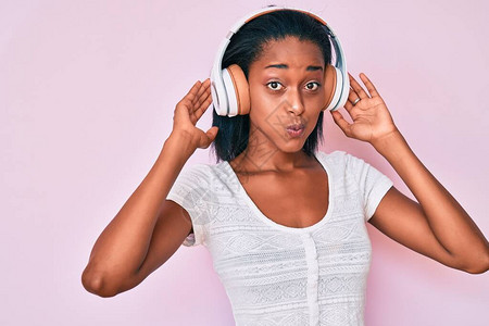 听音乐的年轻非洲女使用耳机用滑稽的脸朝部吹图片