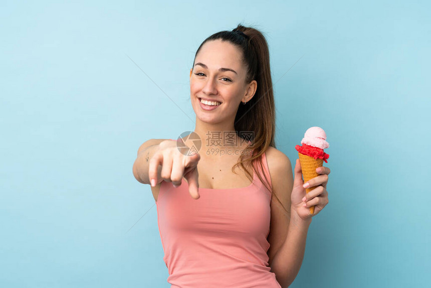 青红头发的年轻女人带着一个玉米角冰淇淋在孤立的蓝色背景点上用自信图片
