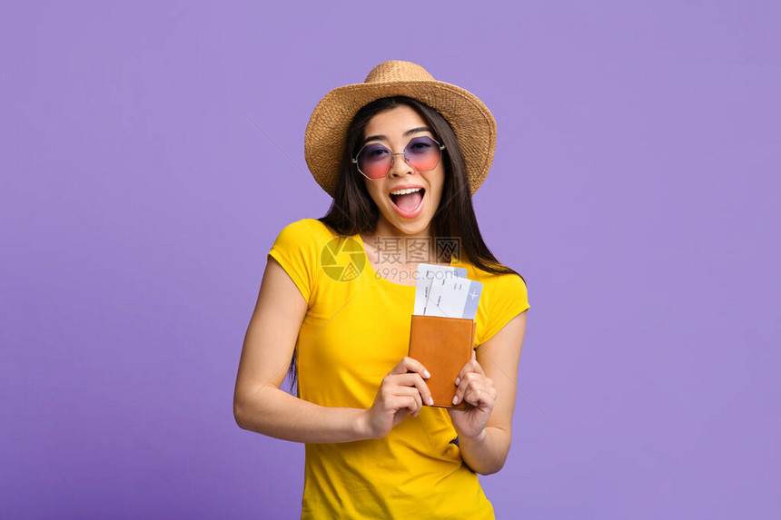 兴奋的亚洲旅游女孩拿着护照和票在紫色背景上合影图片