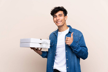 年轻的阿根廷男子在孤立的墙上拿着披萨用拇指举起大拇指因图片