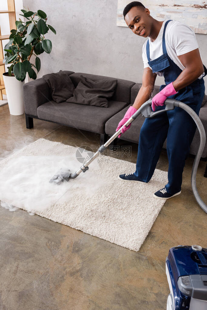 穿着制服和橡胶手套的非洲裔美国清洁工在用热蒸汽清洁地毯时图片