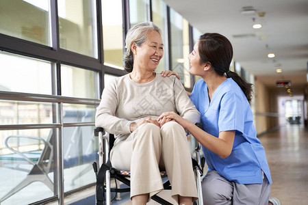 在走廊与亚洲高龄妇女交谈的疗养院护理人图片