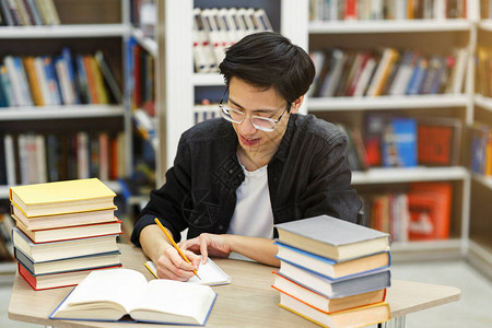 亚洲男学生在公共图书馆写笔记本图片