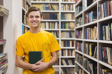知识欢快的白人男学生站在校园图书馆架之间图片