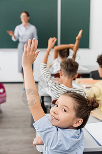 女学生手在空中看着同学和背景老师附近的相机图片