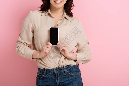 以粉红背景的空白屏幕持智能手机的笑脸褐色女图片