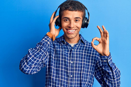 年轻的非洲美国人用耳机收听音乐用手指做好标记微笑着的友善手势模范图片
