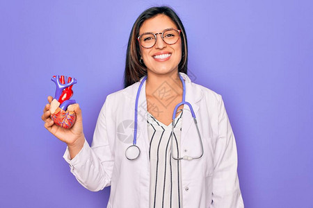 年轻的心脏病学专家女在紫色的背景中拿着医疗心脏图片