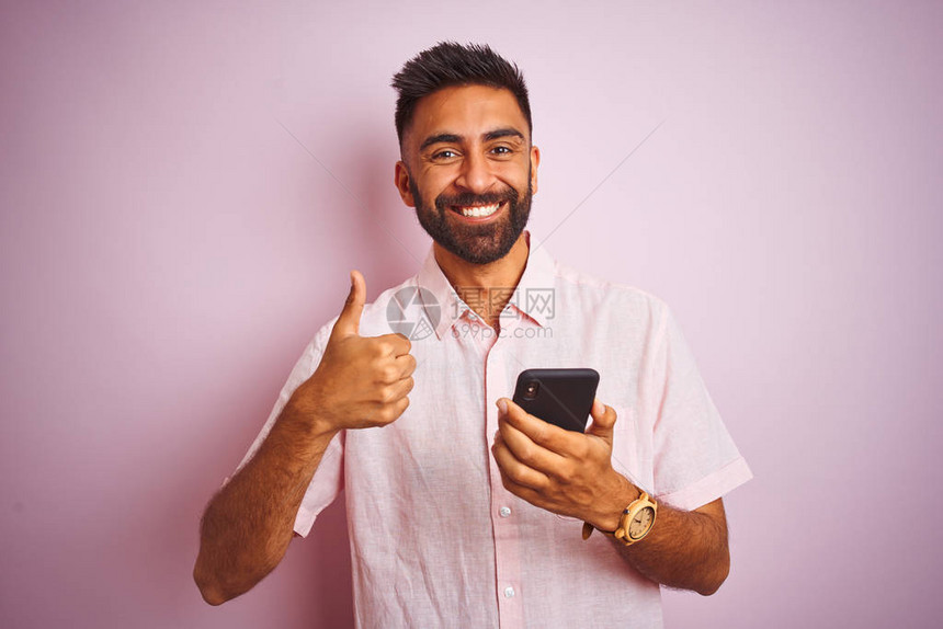 年轻的印度男子用智能手机站在孤立的粉红色背景上图片