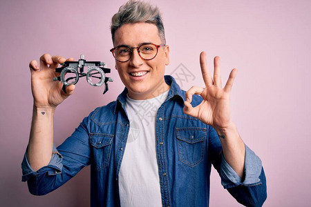 年轻的现代光学验光师男子在粉红色背景上拿着验光眼镜图片