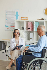 在诊所咨询期间微笑的女医生咨询坐在轮椅上的残疾老人的肖像图片