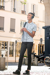 微笑的年轻人站在外面用手机和耳机听音乐的全长肖像图片