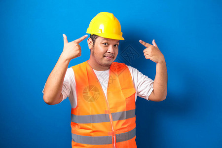 亚洲建筑工人穿着橙色安全背心和蓝色背景头盔图片