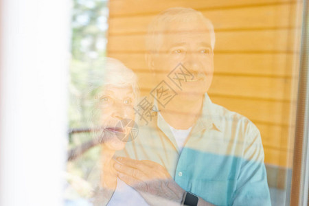 当代亲情的老年配偶站在其住房窗口旁图片