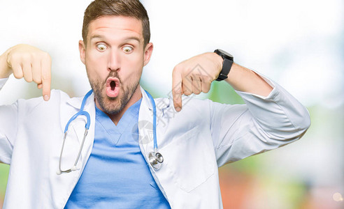 英俊的医生在孤立的背景下穿着医疗制服用手指向下指着广告惊讶的图片