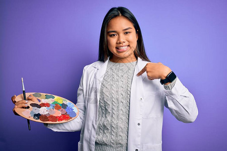 年轻的亚洲女艺术家画用油漆刷和调色板用彩色涂在紫色背景上惊讶的图片