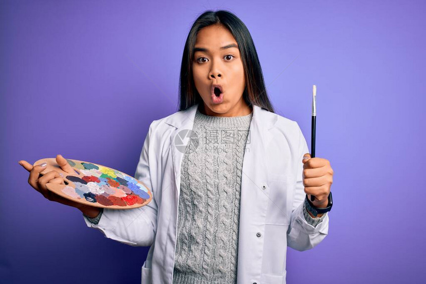 年轻的亚洲艺术家女孩用画笔和调色板在紫色背景上作画图片