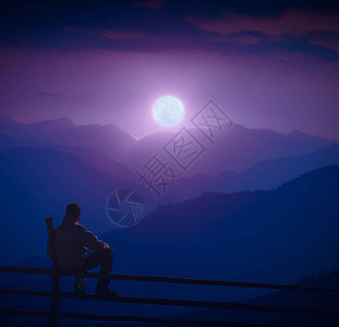 男人坐在木栅栏上享受满月在山谷上图片