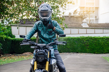 穿着绿色皮夹克的快乐的亚洲人肖像在城市街道骑摩托图片