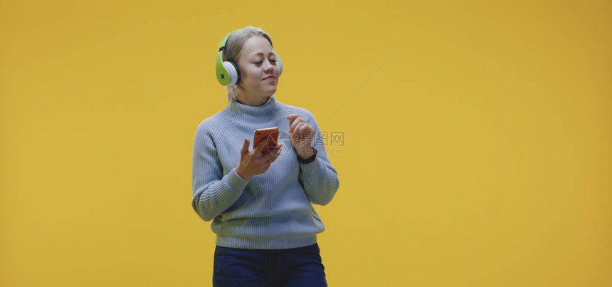 女在黄色背景下从智能手机中听音乐时跳舞的中度镜头图片