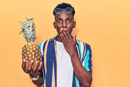身着夏衣和墨镜的年轻非洲男子手拿菠萝盖住嘴图片