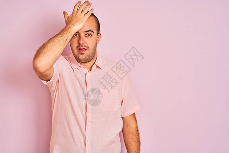 穿着优雅衬衫站在孤立的粉红色背景上的年轻人因错误而惊讶地用手捂着头图片