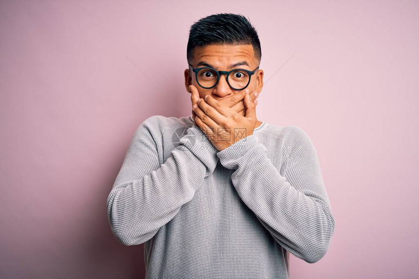 穿着随身毛衣和眼镜的年轻帅哥拉丁男子在粉红背景上被用手顶住图片