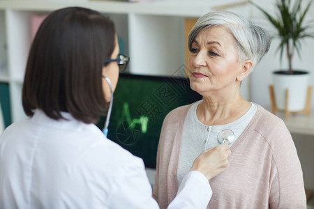 女医生在诊所会诊时通过胸前听诊器听老年妇女心脏图片