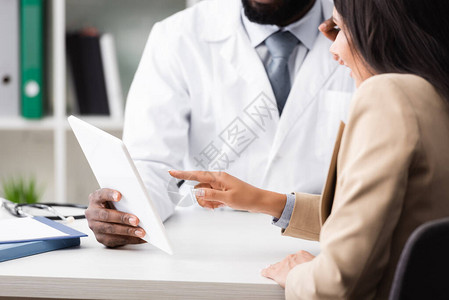在病人用手指对准病人附近持有数字石板的非裔美国医生的作图片